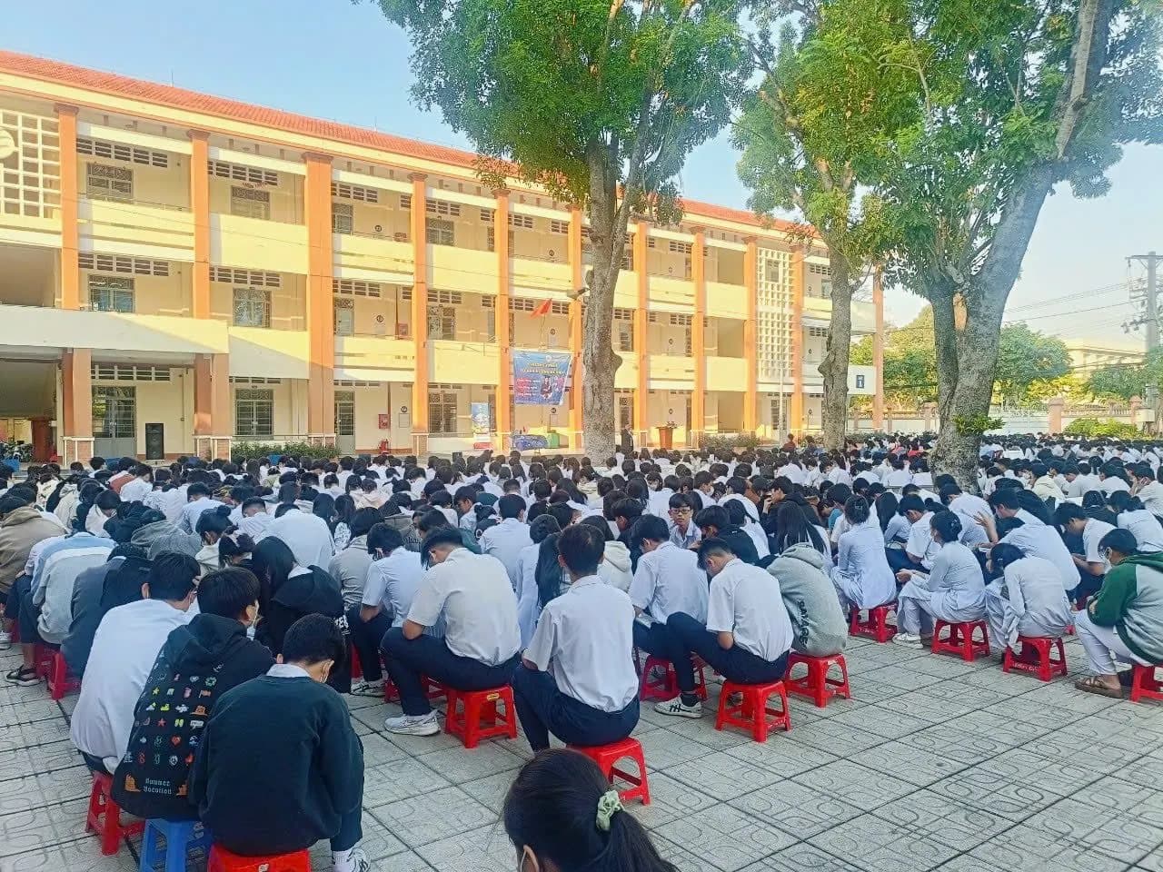 Học sinh ngồi trên ghế nhựa đỏ kín sân trường trong nắng sớm