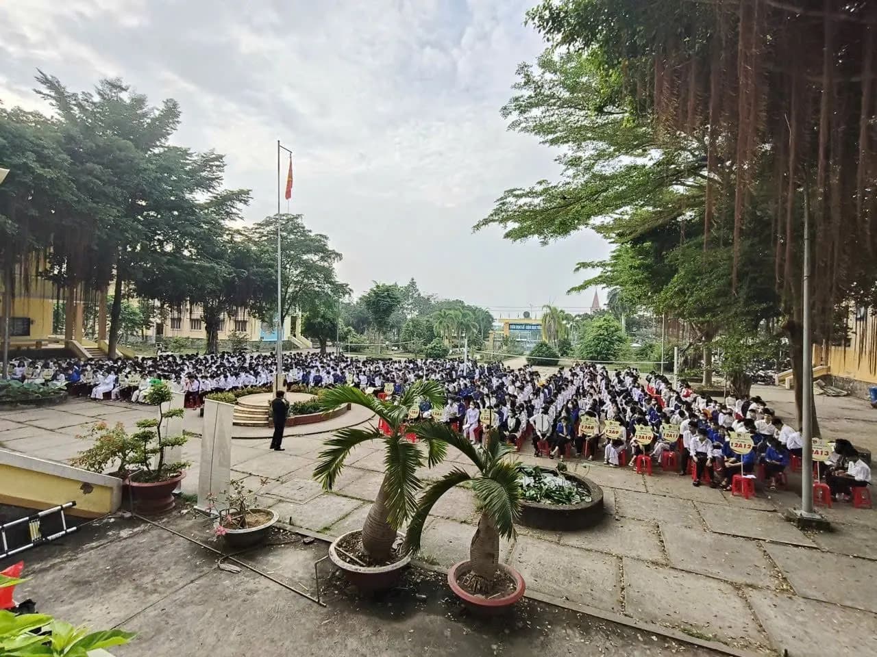 Nhìn từ trên cao: học sinh ngồi kín sân trường quanh cột cờ